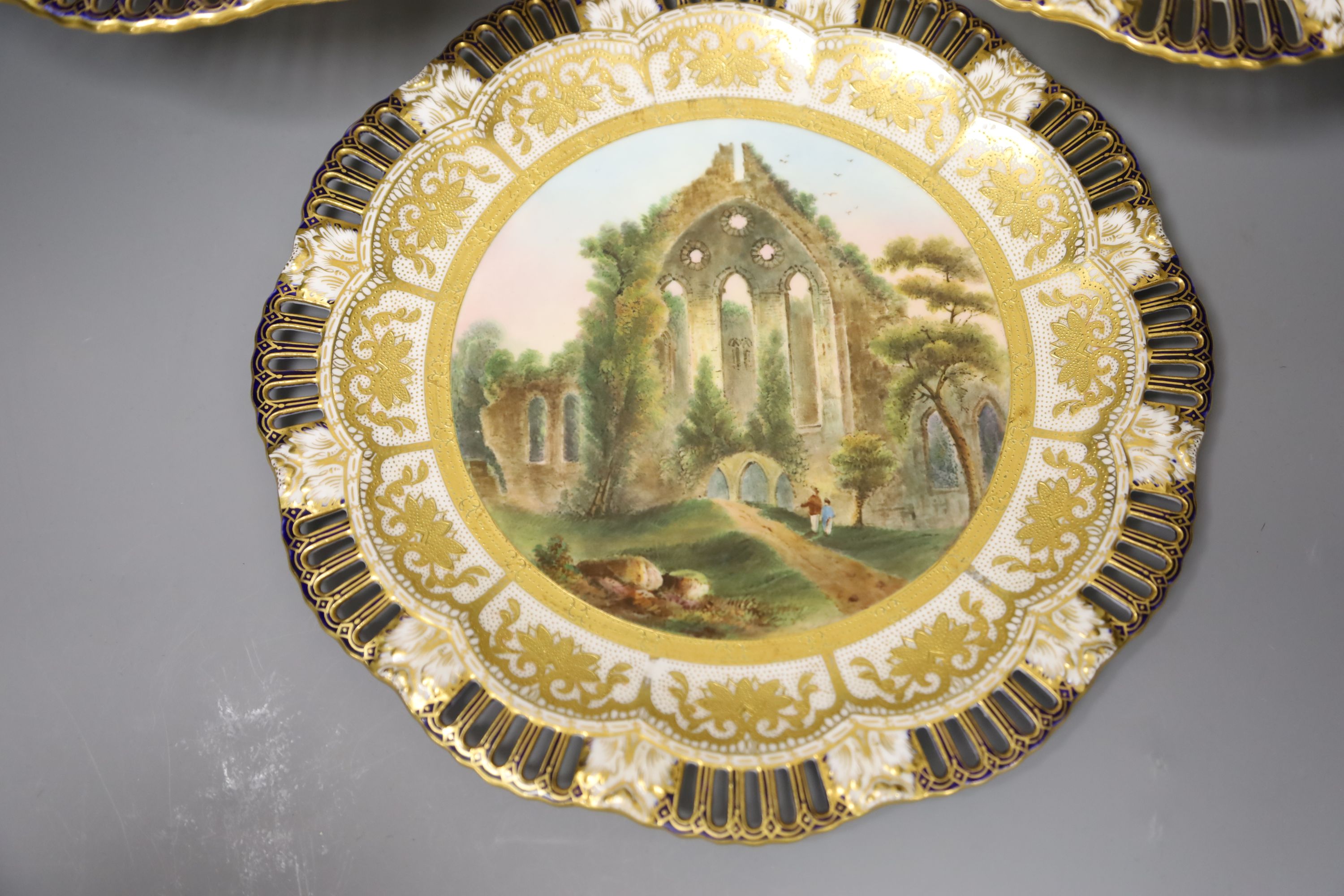 A Coalport plate painted with a titled landscape, diameter 23.5cm, and two comport ensuite all have pierced borders, mark Coalport AD17